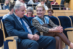 Dwie osoby, mężczyzna i kobieta, siedzące obok siebie podczas rozmowy. W tle uczestnicy wykładu.