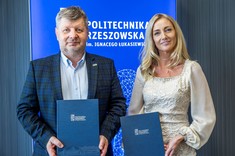 Od lewej rektor, prof. P. Koszelnik, dr. B. Szafrańska. Dwie osoby, kobieta i mężczyzna stoją obok siebie, delikatnie się uśmiechają. Oboje prezentują podpisane umowy.  W tle niebieski baner z białym napisem Politechnika Rzeszowska.