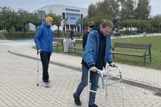 Zdjęcie na zewnątrz, widoczni studenci poruszający się o kulach, z zasłoniętymi oczami wraz z laską dla osób niewidomych oraz student poruszający się przy pomocy chodzika/balkonika dla osób starszych. 