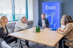 Osoby zgromadzone podczas podpisania umowy podczas swobodnej rozmowy. Pięć osób, cztery kobiety i jeden mężczyzna siedzi wokół stołu na tle przeszklonej ściany. 