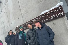 Zdjęcie kilku studentów na zewnątrz budynku pod napisem: Muzeum Sztuki Współczesnej w Krakowie, umieszczonym na betonowej ścianie . Biały napis na ciemnym tle. Zdjęcie wykonane zimą.