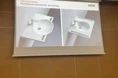 Na zdjęciu ekran z wyświetloną prezentacją. Na slajdzie widoczne dwie białe umywalki z bocznymi uchwytami dla osób z niepełnosprawnościami. 