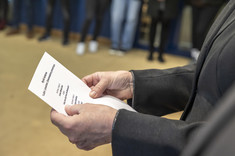 Zbliżenie na kartkę z czarnymi napisami trzymaną w rękach.