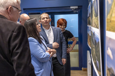 Kilka osób zgromadzonych przy planszach z fotografiami zawieszonymi na ciemnej ścianie. Przyglądają się uważnie szczegółom zdjęć.