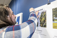 Mężczyzna z długimi włosami wiesza na planszy opis do zdjęcia.