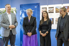 Cztery osoby: dwóch mężczyzn po bokach i po środku dwie kobiety stoją obok siebie. Mężczyzna po lewej przemawia. W tle plansza ze zdjęciami.