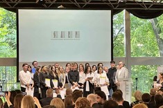 Kolorowe zdjęcie przedstawia osoby zgromadzone podczas gali wręczenia nagród. Publiczność widoczna na pierwszym planie jest ustawiona tyłem do zdjęcia, w dalszym planie na scenie zgromadzeni wszyscy finaliści konkursu, ubrani w biało-czarne stroje.