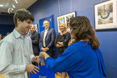 Student, młody mężczyzna w jasnej koszuli odbiera nagrodę od kobiety w jasno granatowej sukience, fot. B.Motyka 