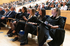 Duża grupa osób siedzących w rzędach podczas wykładu. Na pierwszym planie cztery kobiety ubrane na czarno. 