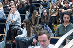 Zbliżenie na słuchaczy wykładu siedzących na schodach.