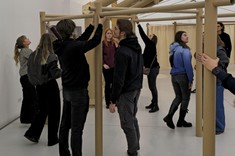 We wnętrzu grupa kilkunastu młodych osób w trakcie budowy szkieletu budynku z tub papierowych.