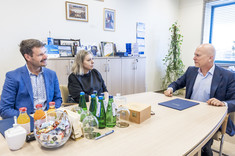Trzy osoby dwóch mężczyzn i kobieta po środku siedzą przy stole podczas spokojnej rozmowy. Uśmiechają się.