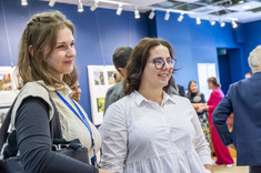 Zdjęcie grupy osób na tle wystawy. Na pierwszym planie dwie kobiety, uśmiechają się do zdjęcia.