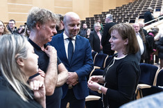 Na pierwszym planie grupa czterech osób podczas swobodnej rozmowy, dwie kobiety i mężczyzna ubrani na czarno i mężczyzna w ciemnym garniturze.