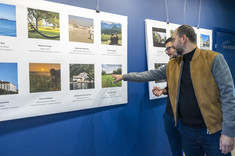 Dwóch mężczyzn z ciemnymi włosami i brodami przygląda się wystawie. Jeden z nich wskazuje jedno ze zdjęć ręką.