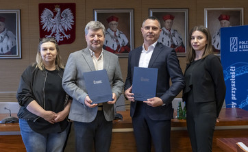 Na zdjęciu stoją obok siebie cztery osoby, dwóch mężczyzn i dwie kobiety po lewej i prawej stronie.  Mężczyźni trzymają w ręku dokumenty.