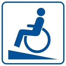 Symbol osoby z niepełnosprawnością ruchu. Osoba na wózku wjeżdża po nachyleniu terenu. Niebieski symbol na białym tle.