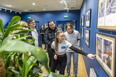 Grupa studentów przygląda się fotografiom wiszącym na ścianie,