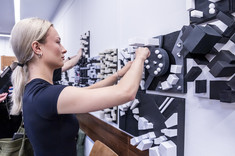 Kobieta ubrana na czarno przypina do białej tablicy biało-czarną makietę.