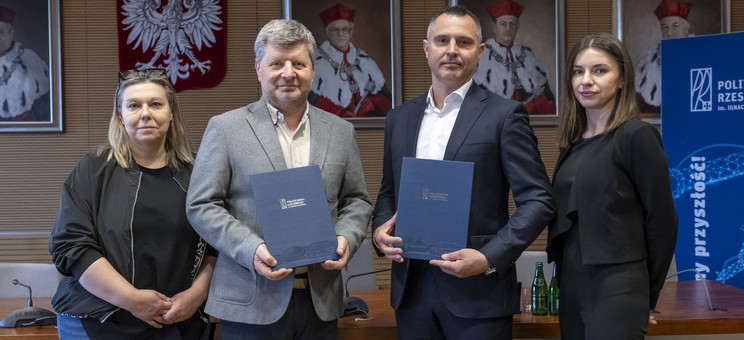 Na zdjęciu stoją obok siebie cztery osoby, dwóch mężczyzn i dwie kobiety po lewej i prawej stronie.  Mężczyźni trzymają w ręku dokumenty.  