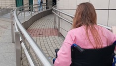 Kobieta w różowej bluzce, wjeżdżająca na wózku inwalidzkim po rampie.