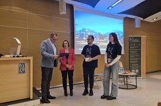 W pomieszczeniu z przyciemnionym światłem stoją cztery osoby. Po lewej mężczyzna w jasnej marynarce przygląda się trzymanemu w rękach dokumentowi. W tle ściana z drewnopodobnym wykończeniem i ekran z wyświetlonym zdjęciem.