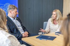 Osoby zgromadzone podczas podpisania umowy podczas swobodnej rozmowy. Po środku mężczyzna i kobieta siedzą przy stole podczas rozmowy. 