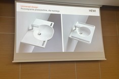 Na zdjęciu ekran z wyświetloną prezentacją. Na slajdzie widoczne dwie białe umywalki z bocznymi uchwytami dla osób z niepełnosprawnościami. 