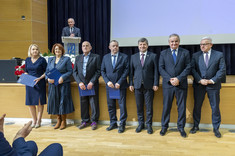 Na zdjęciu w rzędzie stoi siedem osób oficjalnie ubranych. Dwie kobiety od lewej i pięciu mężczyzn.