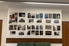 W pomieszczeniu na jasnej ścianie około dwudziestu zdjęć w stonowanych barwach rozplanowanych na prostokątnych planszach. W górnym lewym rogu kolorowy plakat wystawy.