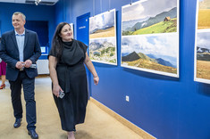 Mężczyzna i kobieta ubrani na ciemno idą wzdłuż ściany z zawieszonymi planszami, przyglądają się prezentowanym fotografiom.