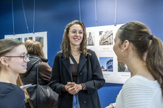 Trzy młode kobiety podczas rozmowy.  W tle plansze ze zdjęciami.