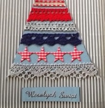 Kartka świąteczna. Na srebrnym tle wycięty prosty, trójkątny niebieski kształt choinki. Na trójkącie umieszczone równoległe poziome pasy z szarej, granatowej i czerwonej koronki. Na czubku choinki szara gwiazda. Pod spodem napis: Wesołych Świat.