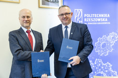 Na zdjęciu widzimy dwóch mężczyzn ubranych w eleganckie garnitury, którzy trzymają teczki z logo Politechniki Rzeszowskiej im. Ignacego Łukasiewicza. Zdjęcie dokumentuje podpisanie umowy.